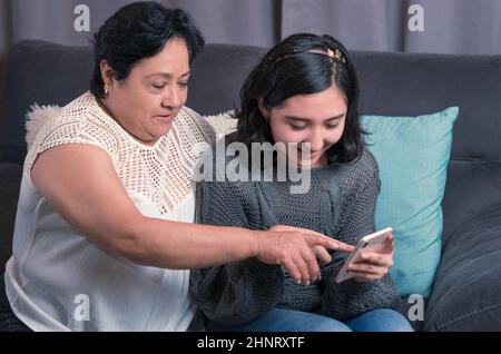 Ältere Frau 60 Jahre alte lateinische Großmutter mit Handy und Spaß mit ihrer Enkelin fotografieren und Videos ansehen Stockfoto