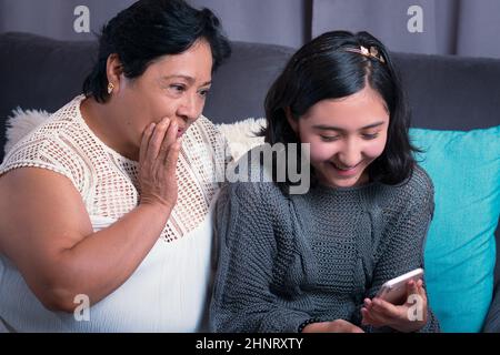 Ältere Frau 60 Jahre alte lateinische Großmutter mit Handy und Spaß mit ihrer Enkelin fotografieren und Videos ansehen Stockfoto