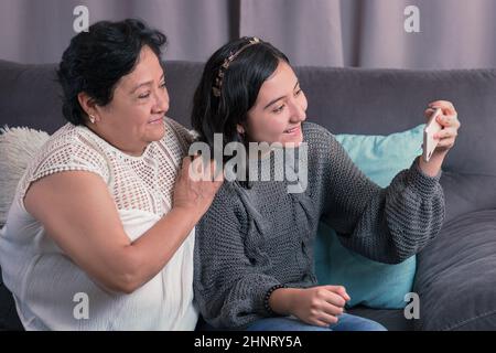 Ältere Frau 60 Jahre alte lateinische Großmutter mit Handy und Spaß mit ihrer Enkelin fotografieren und Videos ansehen Stockfoto