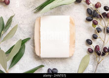 Handgemachte Seifenbar auf einem Marmortisch mit Papierverpackung mit Olivenzweigen um den Tisch herum, Draufsicht. Seifenmockup Mittelmeer flaches Lay, Healt Stockfoto
