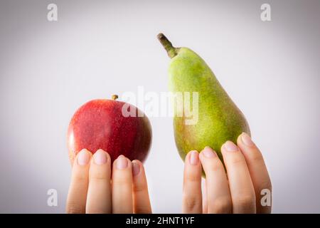 Roter und grüner Apfel und Birne in weiblichen Händen gehalten. Konzeptionell für Vergleich, Differenzierung und Auswahlverfahren. Stockfoto