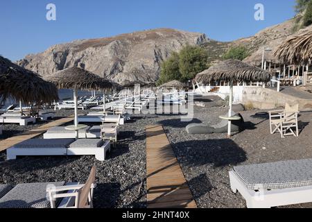 Sonnenliegen am schwarzen Vulkanstrand von Kamari in Santorini. Kykladen, Griechenland Stockfoto