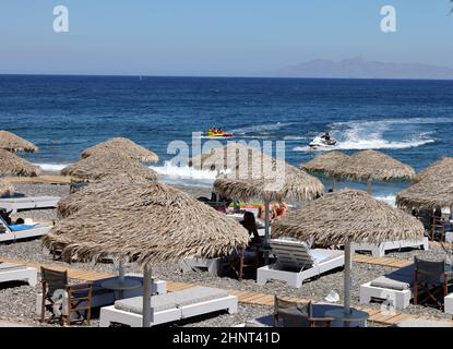 Sonnenliegen am schwarzen Vulkanstrand von Kamari in Santorini. Kykladen, Griechenland Stockfoto