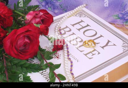 Rosen mit Bibel und Eheringen auf Holztisch Stockfoto