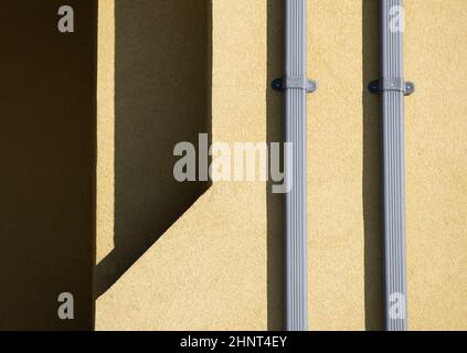 Formen und Muster aus Schatten, die durch das Sonnenlicht am Nachmittag auf die Außenfassade von zwei silbernen Metallausbrüchen auf gelbe Zement- oder Betonwände geworfen wurden Stockfoto