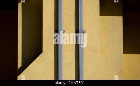 Formen und Muster aus Schatten, die durch das Sonnenlicht am Nachmittag auf die Außenfassade von zwei silbernen Metallausbrüchen auf gelbe Zement- oder Betonwände geworfen wurden Stockfoto