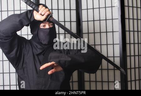 Asian man trägt Ninja Kostüm und hält Ninja Waffen Stockfoto