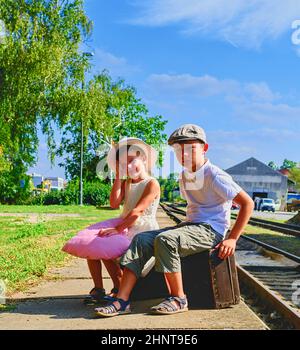 Adorable kleinen Mädchen und Jungen auf einem Bahnhof und warten auf den Zug mit Vintage Koffer. Reisen, Urlaub und chilhood Konzept. Reiseversicherung Konzept. Urlaub Reise Stockfoto