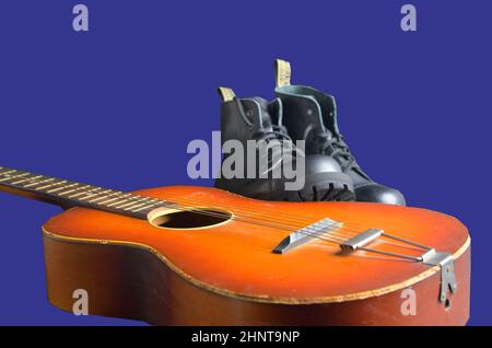 Rock und Roll Konzept. Schwarze Stiefel und akustischer Gitarre. Rock und Roll Stiefel auf marine blau hintergrund Stockfoto