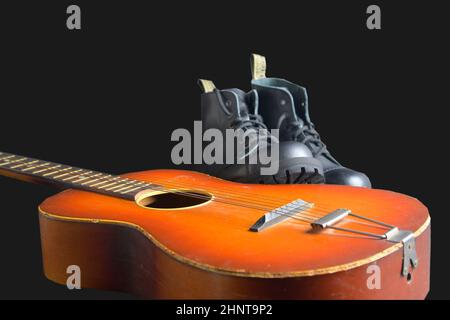 Rock und Roll Konzept. Schwarze Stiefel und akustischer Gitarre. Rock und Roll Stiefel auf schwarzem Hintergrund Stockfoto