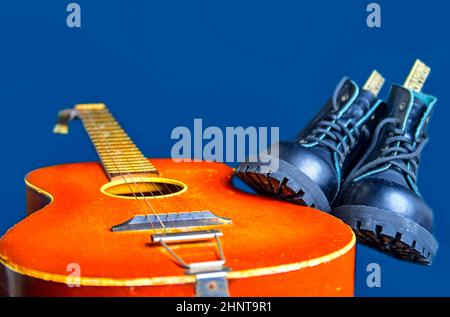 Rock und Roll Konzept. Schwarze Stiefel und akustischer Gitarre. Rock und Roll Stiefel auf marine blau hintergrund Stockfoto