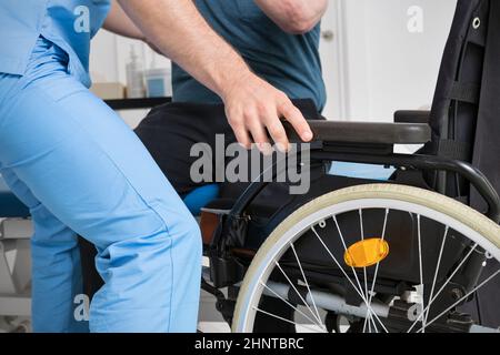 Männlicher Physiotherapeut, der einem Patienten mit einer Behinderung hilft, der einen Rollstuhl benutzt, um im Reha-Krankenhaus aufzustehen. Stockfoto