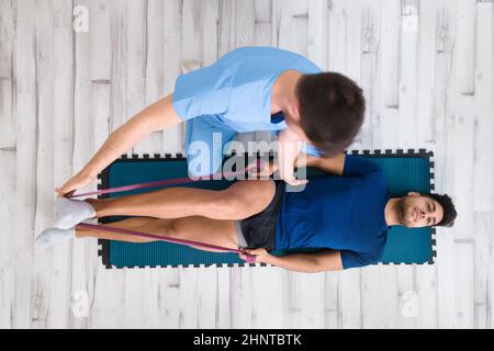 Ansicht von oben eines Therapeuten, der einem männlichen Patienten hilft, während er sein Bein im Krankenhaus streckt Stockfoto