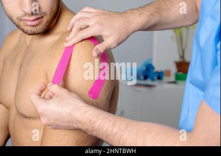 Physiotherapeut, der Kinesioband auf die Schulter des männlichen Patienten aufklebt. Kinesiologie, Physiotherapie, Rehabilitationskonzept. Nahaufnahme Stockfoto