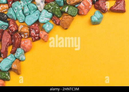 Bonbon-Kieselsteine auf gelbem Hintergrund. Süßigkeiten in Form von farbigen Steinen. Kopierraum Stockfoto