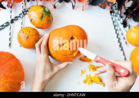 Halloween am 31. Oktober. Der Schritt-für-Schritt-Prozess des Schnitzens eines Kürbisses. Das Mädchen schneidet das Gesicht des Kürbisses mit einem Messer. Blick von oben Stockfoto