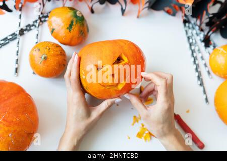 Halloween am 31. Oktober. Der Schritt-für-Schritt-Prozess des Schnitzens eines Kürbisses. Das Mädchen schneidet das Gesicht des Kürbisses mit einem Messer. Blick von oben Stockfoto