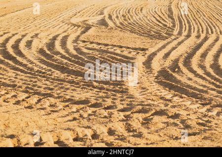 Muster von gebogenen Graten und Furchen auf einem sandigen Feld. Spuren auf dem Sand. Traktorbahnen Stockfoto