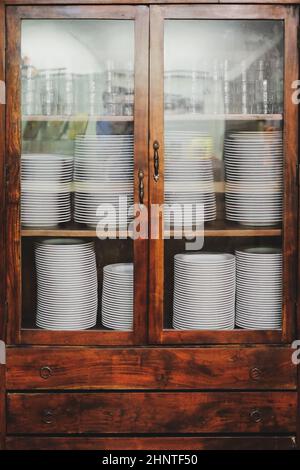 Vintage Schrank mit weißem Geschirr. Alte hölzerne Küchenschrank mit Stapel von weißen Tellern und Tassen. Retro Sideboard Stockfoto