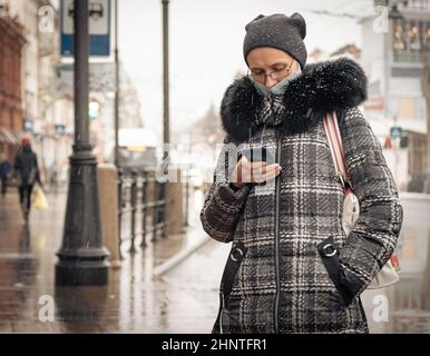 26th. Oktober 2020, Russland, Tomsk, Frau mit Smartphote und Gesichtsmask auf der Straße Stockfoto