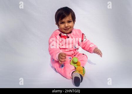 Nahaufnahme Porträt von Happy Baby trägt rosa Samt warme Kleidung auf weißem Hintergrund. Niedliches Baby im Bodysuit Herbst- oder Wintermode-Outfit an einem sonnigen Tag. Ganz kleiner Junge. Speicherplatz kopieren. Vorderansicht Stockfoto