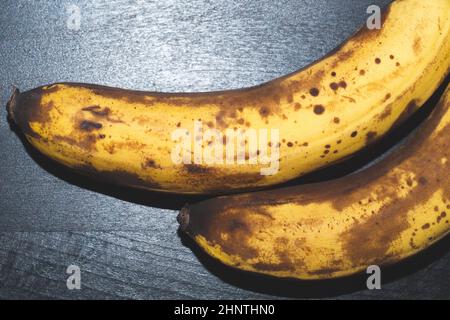 Überreife Bananen mit Flecken. Früchte liegen auf schwarzem Holztisch Stockfoto