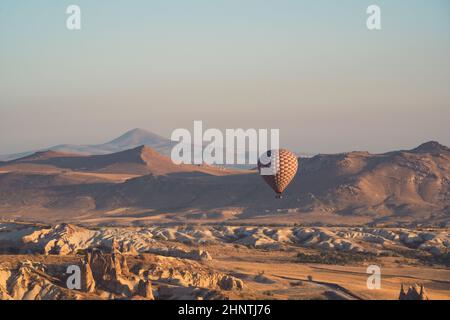 Landschaft mit einsamem Heißluftballon mit kariertem Muster, das im Morgenlicht über das Panorama des Kappadokischen Tals steigt Stockfoto