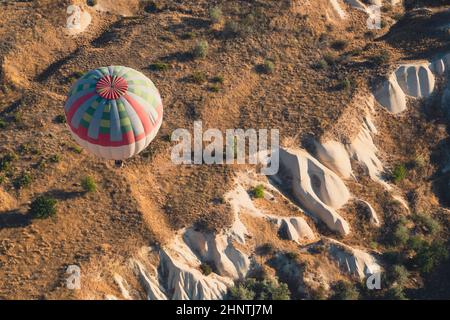Draufsicht Nahaufnahme eines einsamen Heißluftballons mit blauen und roten Farbmustern, die im Morgenlicht über das Panorama des Kappadokischen Tals aufsteigen Stockfoto