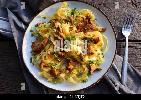 Tagliatelle Pasta mit gebratenen in Butter Pfifferlinge Pilze mit Knoblauch und fein gehackte Petersilie auf karierte Serviette auf einem rustikalen Hintergrund . Obere V Stockfoto