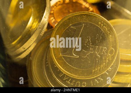 Münzen verschiedener Länder in einem Glasbecher. Viele Metallmünzen verschiedener Stückelungen und verschiedener Länder. Finanzieller Hintergrund. Euro-Münze in Stockfoto