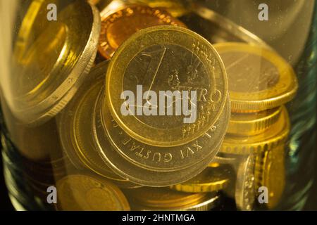 Münzen verschiedener Länder in einem Glasbecher. Viele Metallmünzen verschiedener Stückelungen und verschiedener Länder. Finanzieller Hintergrund. Euro-Münze in Stockfoto