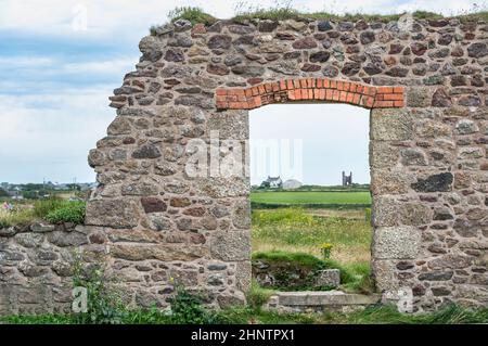 Überreste einer alten Steuerhauswand aus Zinn und einer Öffnung am Eingang, die über Fiele zum Horizont mit anderen entfernten Gebäuden blickt. Stockfoto