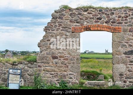 Überreste einer alten Steuerhauswand aus Zinn und einer Öffnung am Eingang, die über Fiele zum Horizont mit anderen entfernten Gebäuden blickt. Stockfoto