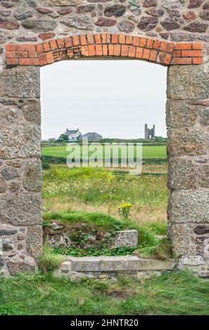 Überreste einer alten Steuerhauswand aus Zinn und einer Öffnung am Eingang, die über Fiele zum Horizont mit anderen entfernten Gebäuden blickt. Stockfoto