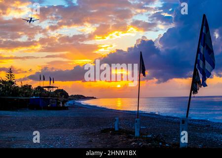 Flaggen vor dem schönsten goldenen Sonnenuntergang und Flugzeug am Horizont am Strand von Ialysos auf der griechischen Insel Rhodos. Stockfoto