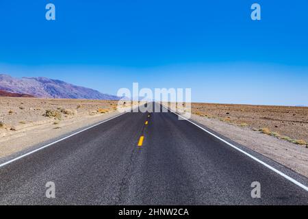 Leere Straße durch die Wüste des Death Valley unter blauem Himmel Stockfoto