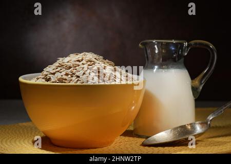 Haferflocken in einer Holzschüssel, Haferflocken und eine Tasse Milch auf dem Tisch. Gesunde Ernährung Stockfoto