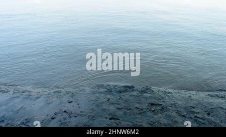 Schlammiges Flussufer bei Ebbe neben Wellenwasser. Vom Fluss abgelagerte Schwemmböden. Natur Hintergrund. Nahaufnahme. Stockfoto