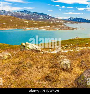 Erstaunliches Vavatn Seenpanorama raue Landschaft Blick Felsen Felsbrocken und Berge mit Schnee im Sommer in Hemsedal Norwegen. Stockfoto