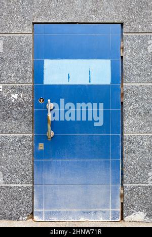 Alte schäbige Eingangstür mit blauer Folie in der Wand des Stadtgebäudes bedeckt mit grauen Granitfliesen Stockfoto