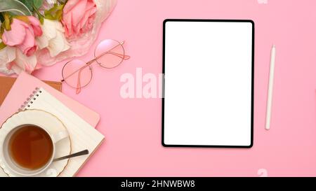 Bürotisch Schreibtisch mit digitalem Tablet-PC mit weißem Bildschirm, Stylus Pen, Brillen, Teetasse, Notizbuch und Rosenstrauß auf rosa Hintergrund. Draufsicht, fl Stockfoto