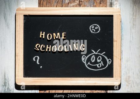 Frontale Nahaufnahme einer kleinen schwarzen Kreidetafel aus Holzbuchstaben mit den Worten Home Schooling und einer Strichfigurenzeichnung aus Kreide auf einem Holz Stockfoto