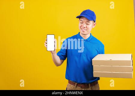Aufgeregt Lieferservice Mann lächelnd trägt blaue Uniform halten Papierbehälter für Mitnehmen Pizzakartons Paket und zeigen Smartphone leeren Bildschirm, Stud Stockfoto