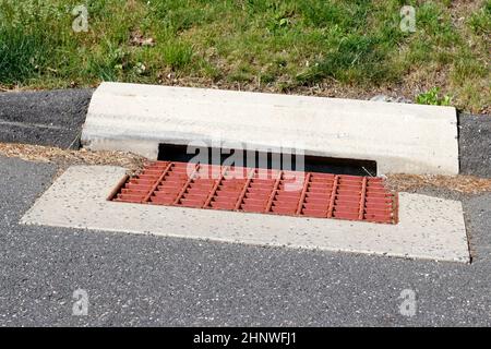 Oberfläche einer Vorstadtstraße rot lackierten Metall Sturm Wasser Grill im Freien am Tag mit Gras im Rücken. Nahaufnahme eines rot lackierten Metallabwasserkanals Stockfoto