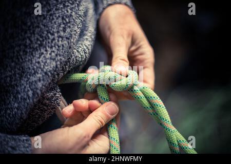 Detail mit den Händen eines Kletterers, der eine Acht an das Geschirr bindet. Stockfoto