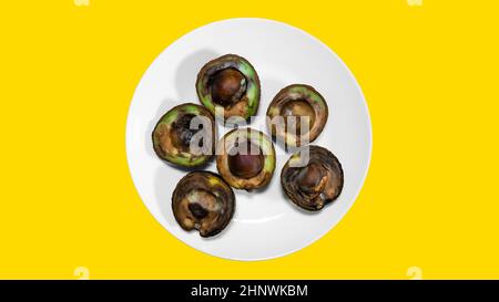 Hässliches Essen auf gelbem Hintergrund. Verfaulte tropische Avocado-Früchte. Konzept der faulen Frucht. Avocado auf einem Teller. Stockfoto