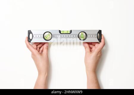 Weibliche Hände halten eine graue metallische Gebäudeebene auf weißem Hintergrund. Messinstrument in rechteckiger Form aus Kunststoff mit transparentem FL Stockfoto