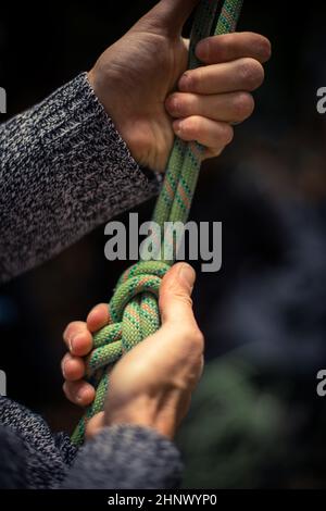 Detail mit den Händen eines Kletterers, der eine Acht an das Geschirr bindet. Stockfoto