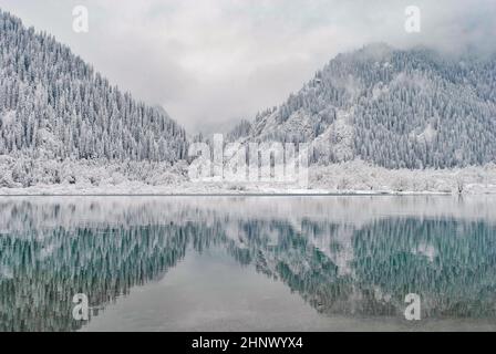 Bergsee im Winter. Schneebedeckte Berge spiegeln sich im Wasser. Winterlandschaft. Stockfoto