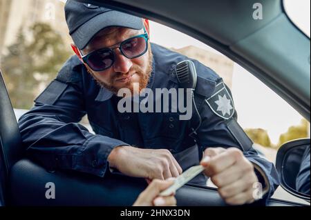 Der männliche Polizist nimmt den Führerschein von einer weiblichen Fahrerin ab. Polizist in Uniform schützen das Gesetz, Registrierung einer Straftat. COP arbeitet in der Stadt Stockfoto